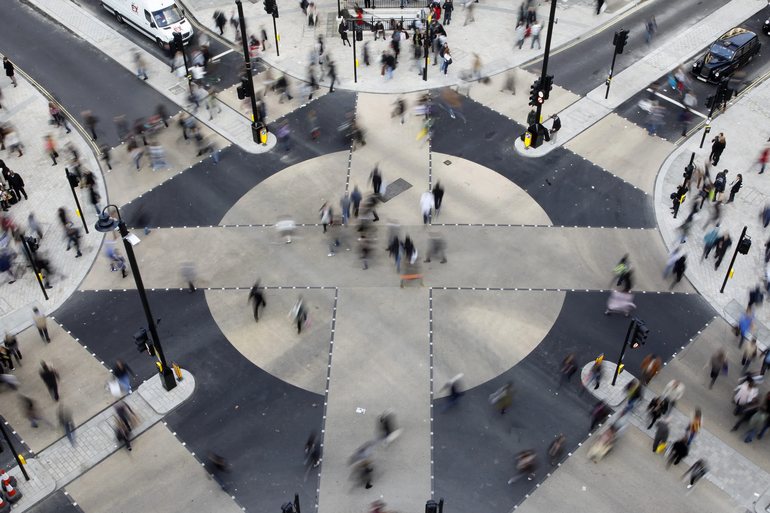 Aerial view of a large city crossing with many pedestrians moving in different directions across zebra crossings.